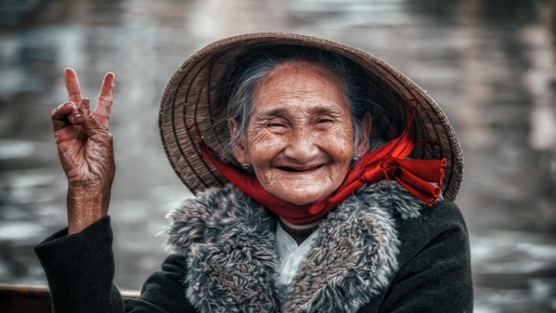 portrait einer älteren asiatisch stämmigen frau mit hut, lächelnd